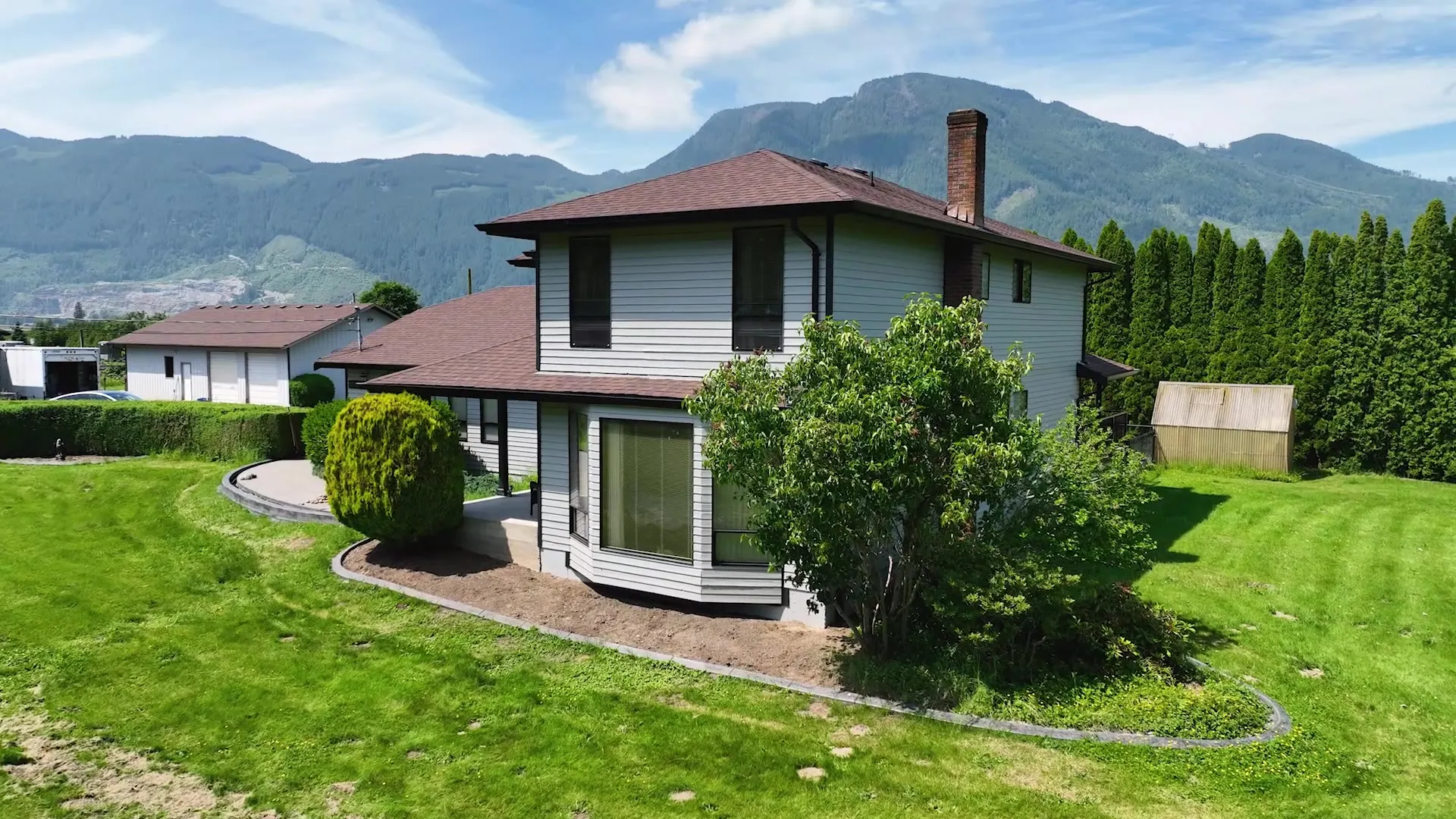 Home with fresh light-grey siding and clean trim after an exterior renovation, framed by mountains